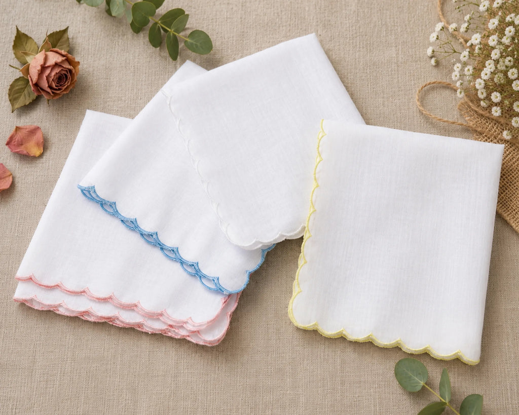 Set of white handkerchiefs with colorful scalloped edges on a beige fabric background.