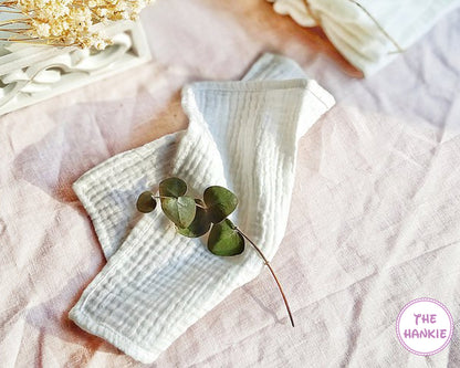White hankie with green leaves on a pink textured surface, brand 'The Hankie' visible.