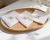 Three embroidered handkerchiefs on a woven tray with flowers in the background