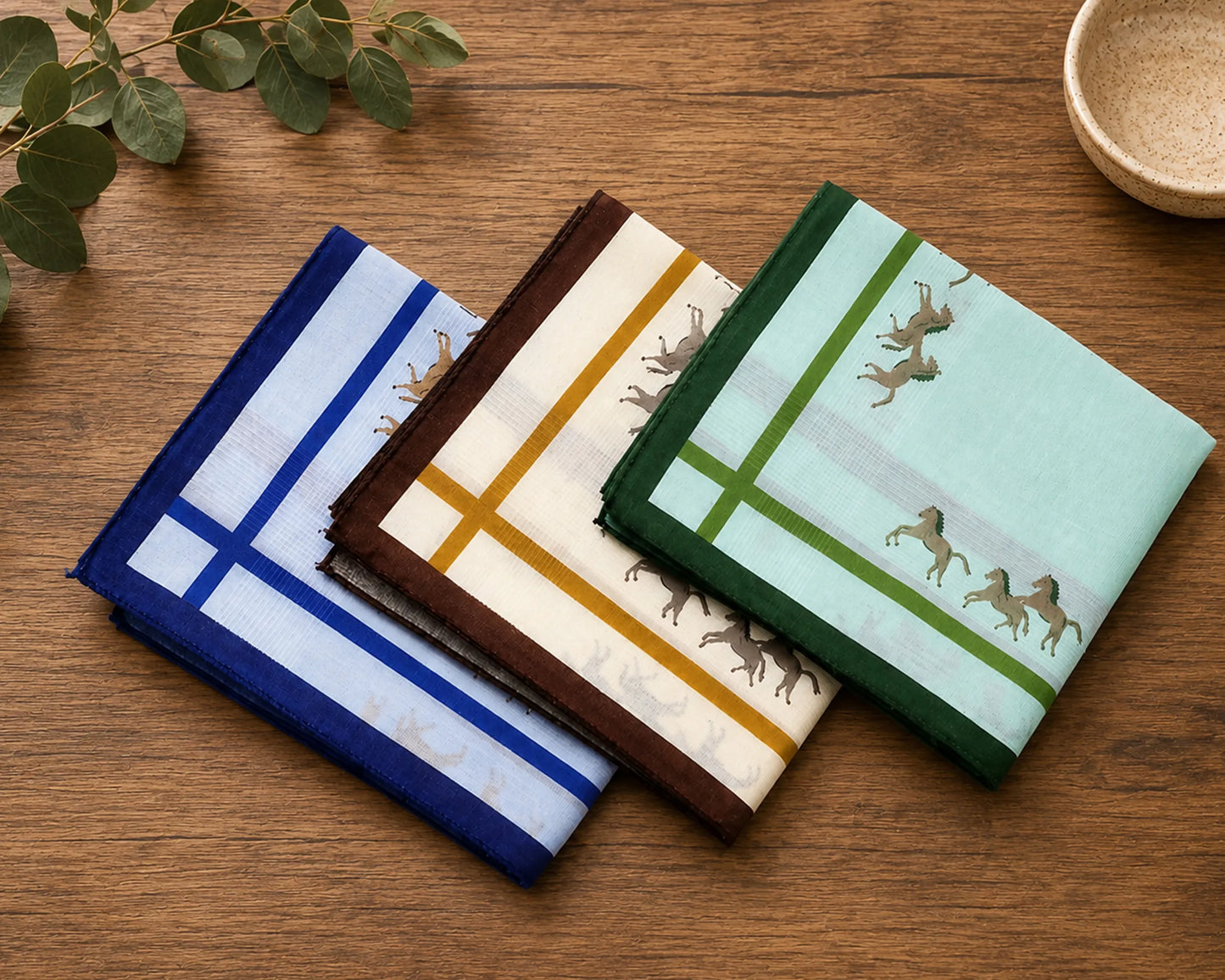 Three patterned hanky on a wooden surface with greenery and a bowl.