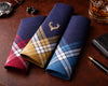 Three plaid pocket squares on a wooden surface with a watch, pen, and glass of whiskey.