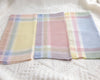 Three plaid handkerchiefs in pastel colors on a white fabric background
