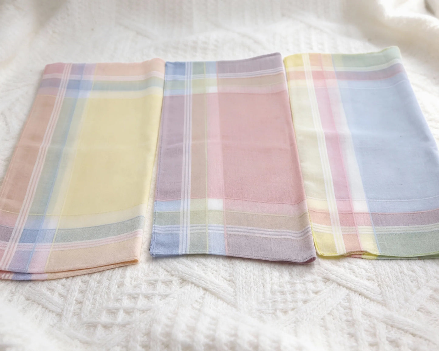 Three plaid handkerchiefs in pastel colors on a white fabric background