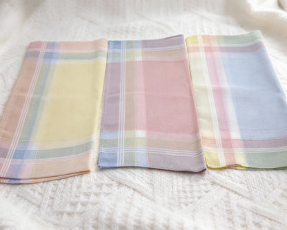 Three plaid handkerchiefs in pastel colors on a white fabric background