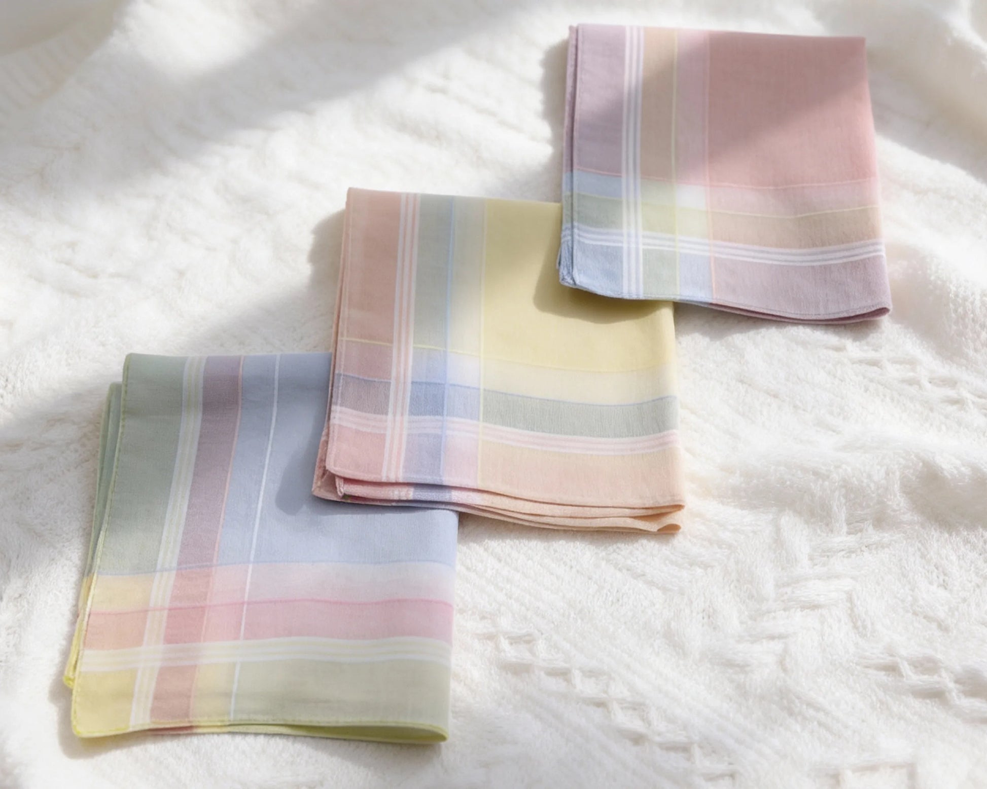 Three plaid hanky in pastel colors on a white textured surface