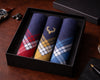 Three plaid pocket squares in a black box on a wooden surface with a watch and pen.
