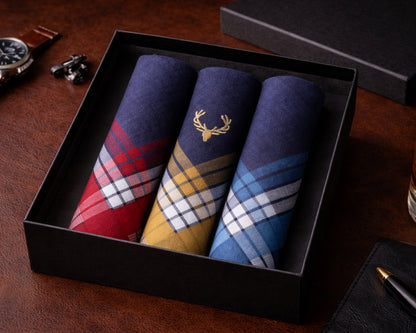Three plaid pocket squares in a black box on a wooden surface with a watch and pen.