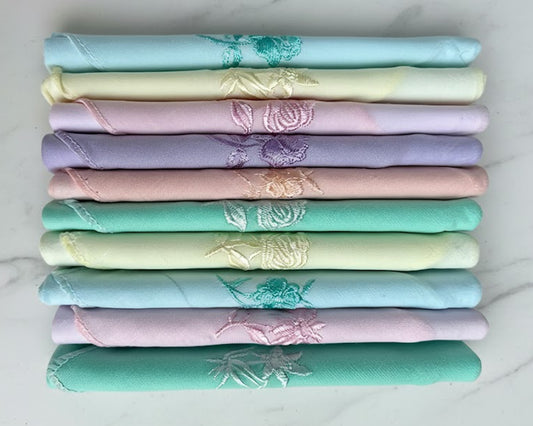 Stack of folded fabric swatches in pastel colors with floral patterns on a white background