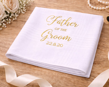 White handkerchief with 'Father of the Groom' text on a wooden surface with flowers and ribbons.