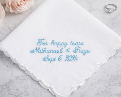 White handkerchief with blue embroidered text on a marble surface with flowers and a ring.
