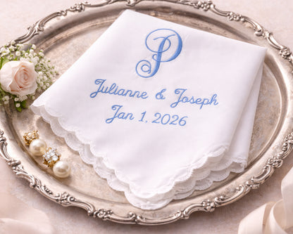 White handkerchief with blue embroidery on a decorative silver tray with flowers and jewelry.