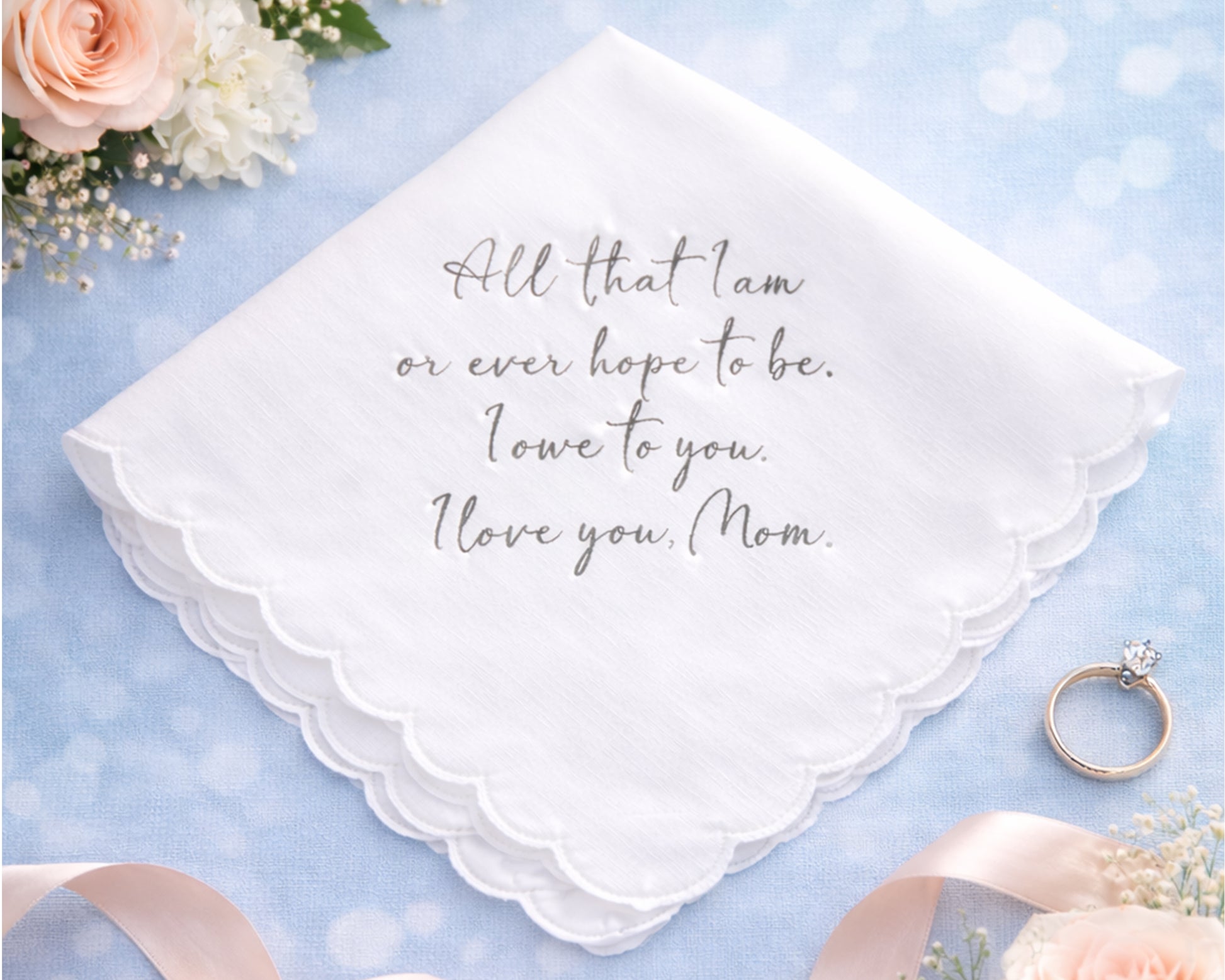 White handkerchief with engraved message on a light blue background with flowers and a ring.