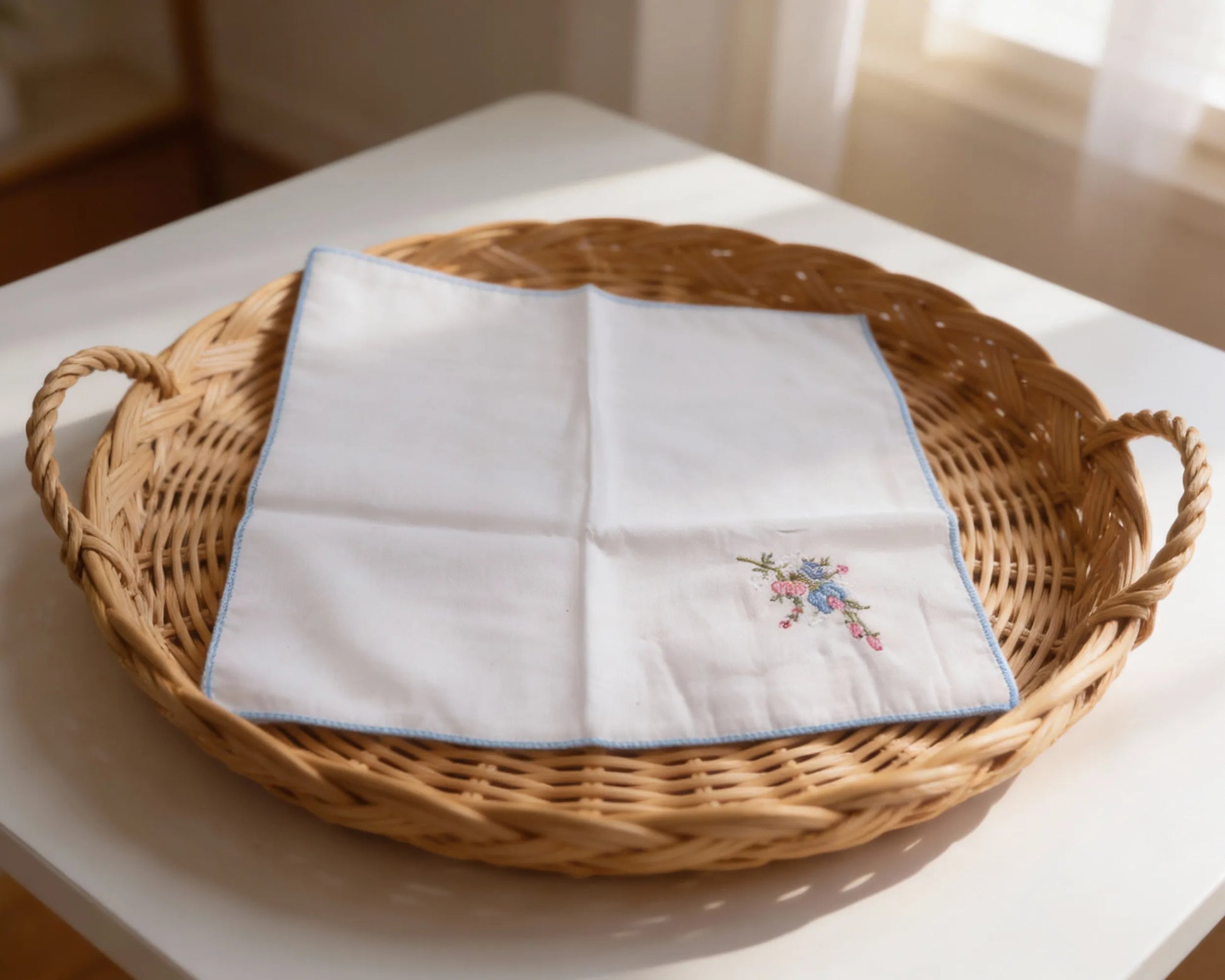 White handkerchief with floral embroidery in a woven basket on a white surface