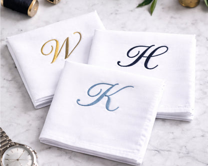 White napkins with embroidered initials 'W', 'H', and 'K' on a marble surface.
