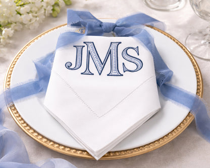 White napkin with 'JMS' monogram on a gold plate with blue ribbon