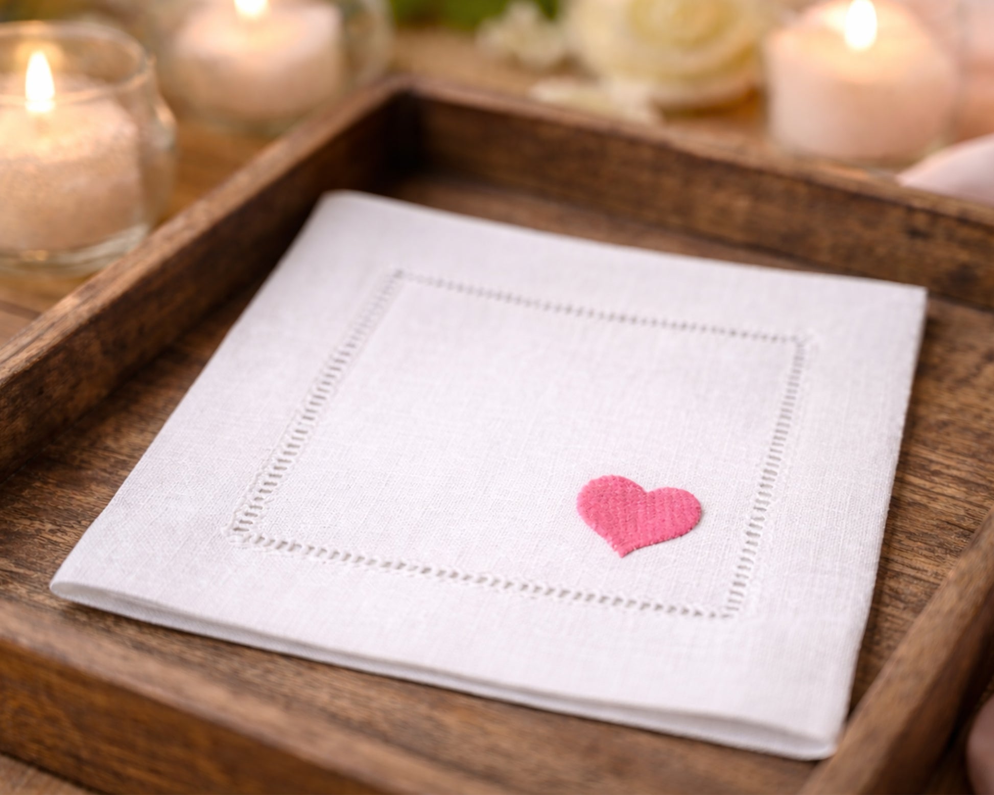 White napkin with a pink heart on a wooden tray with candles in the background