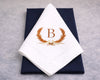 White napkin with gold monogram 'B' design on a navy box against a gray background