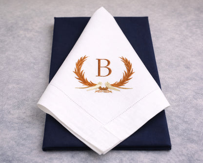 White napkin with gold monogram 'B' design on a navy box against a gray background