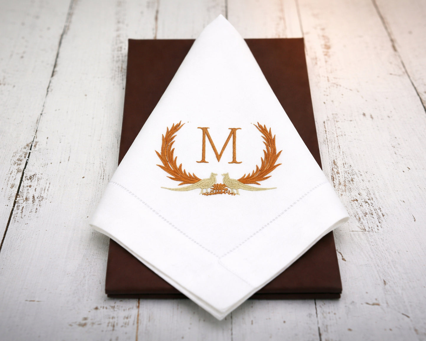 White napkin with gold monogram 'M' design on a brown surface