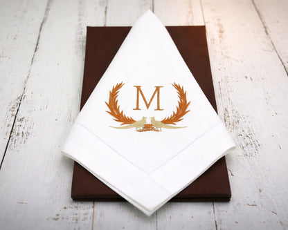 White napkin with gold monogram 'M' design on a brown surface