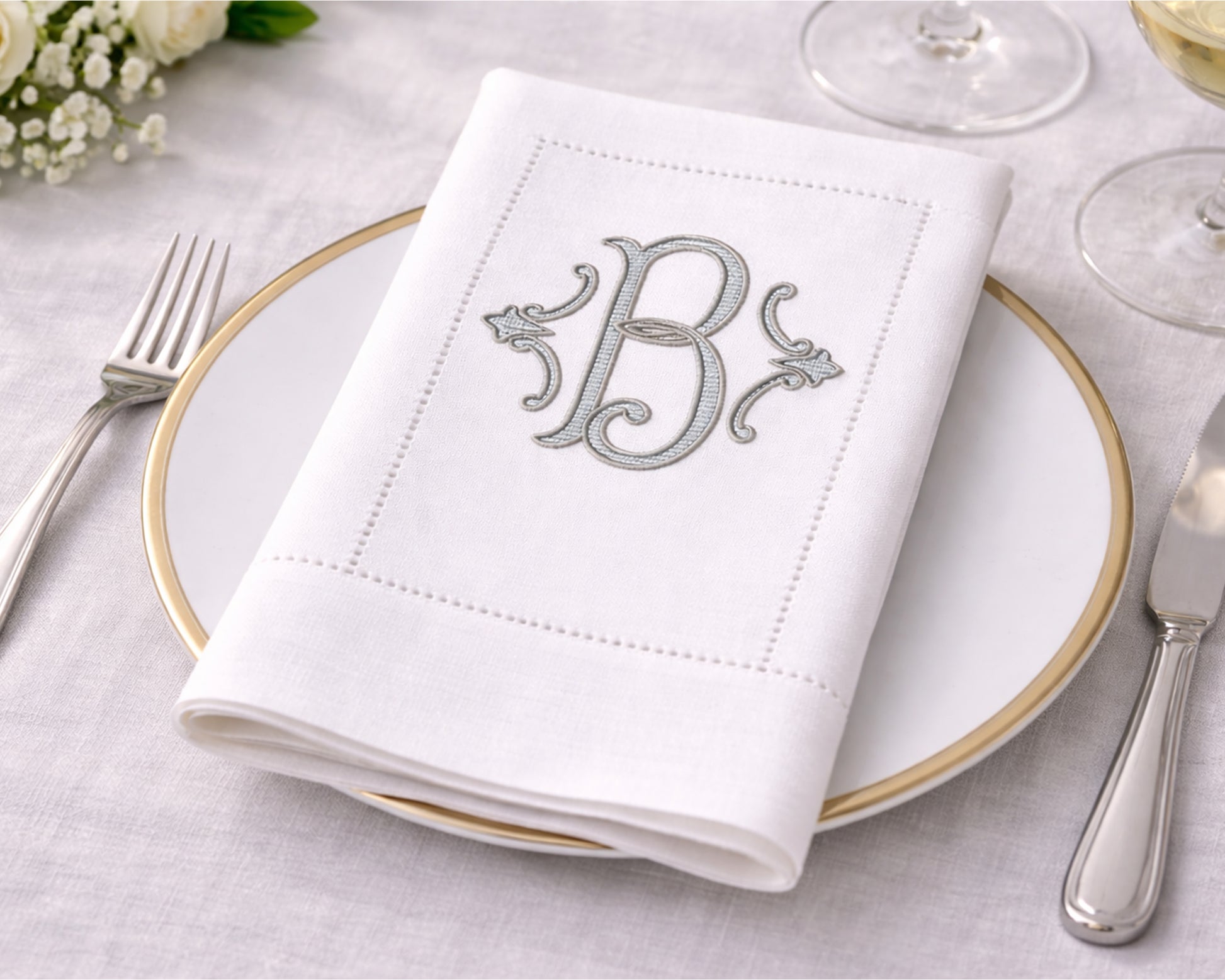 White napkin with monogram 'B' on a table setting with cutlery and glasses.