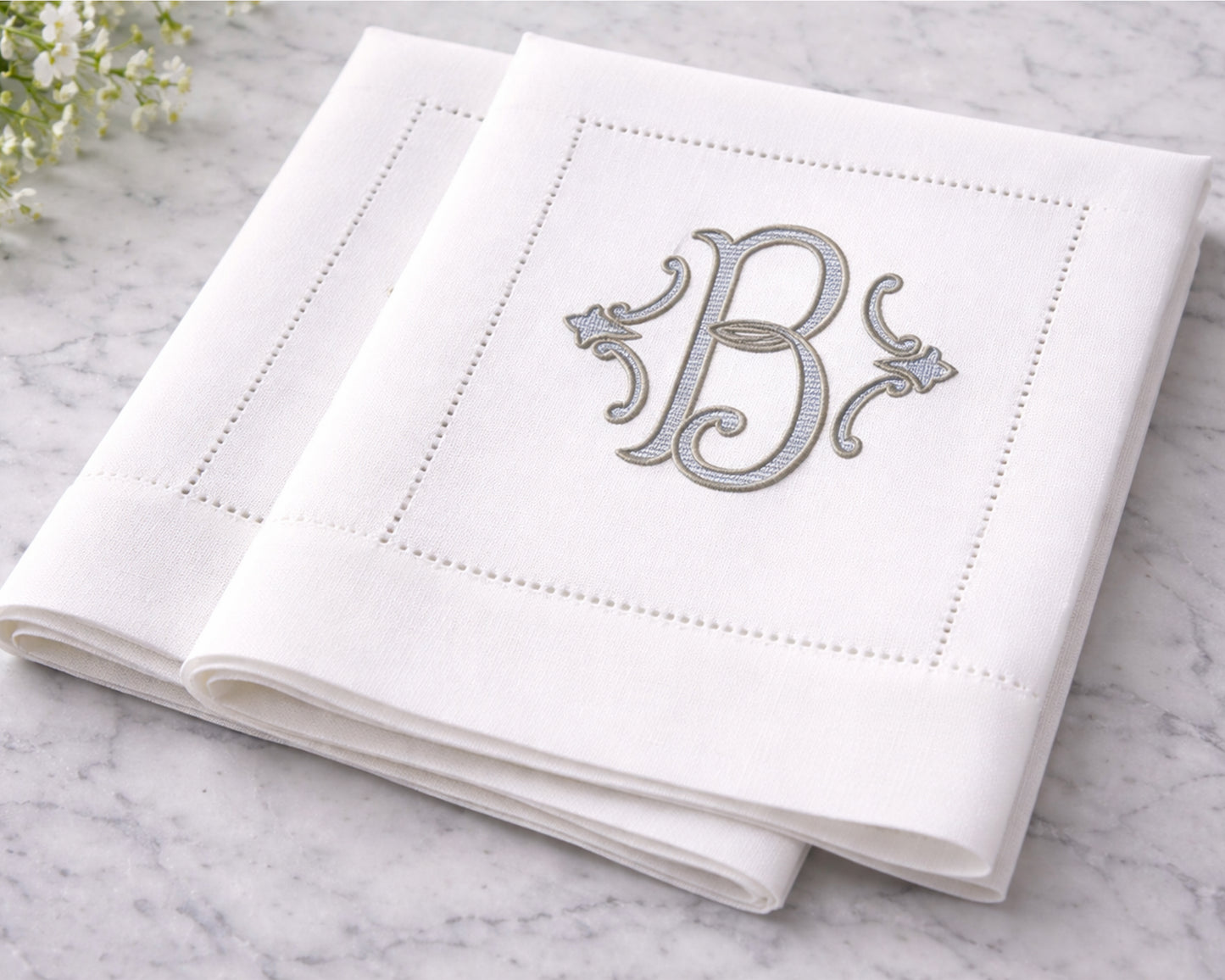 White napkin with silver monogram 'B' on a marble surface