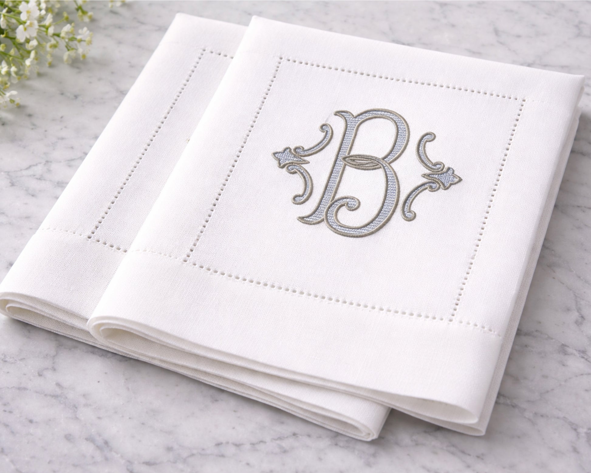White napkin with silver monogram 'B' on a marble surface