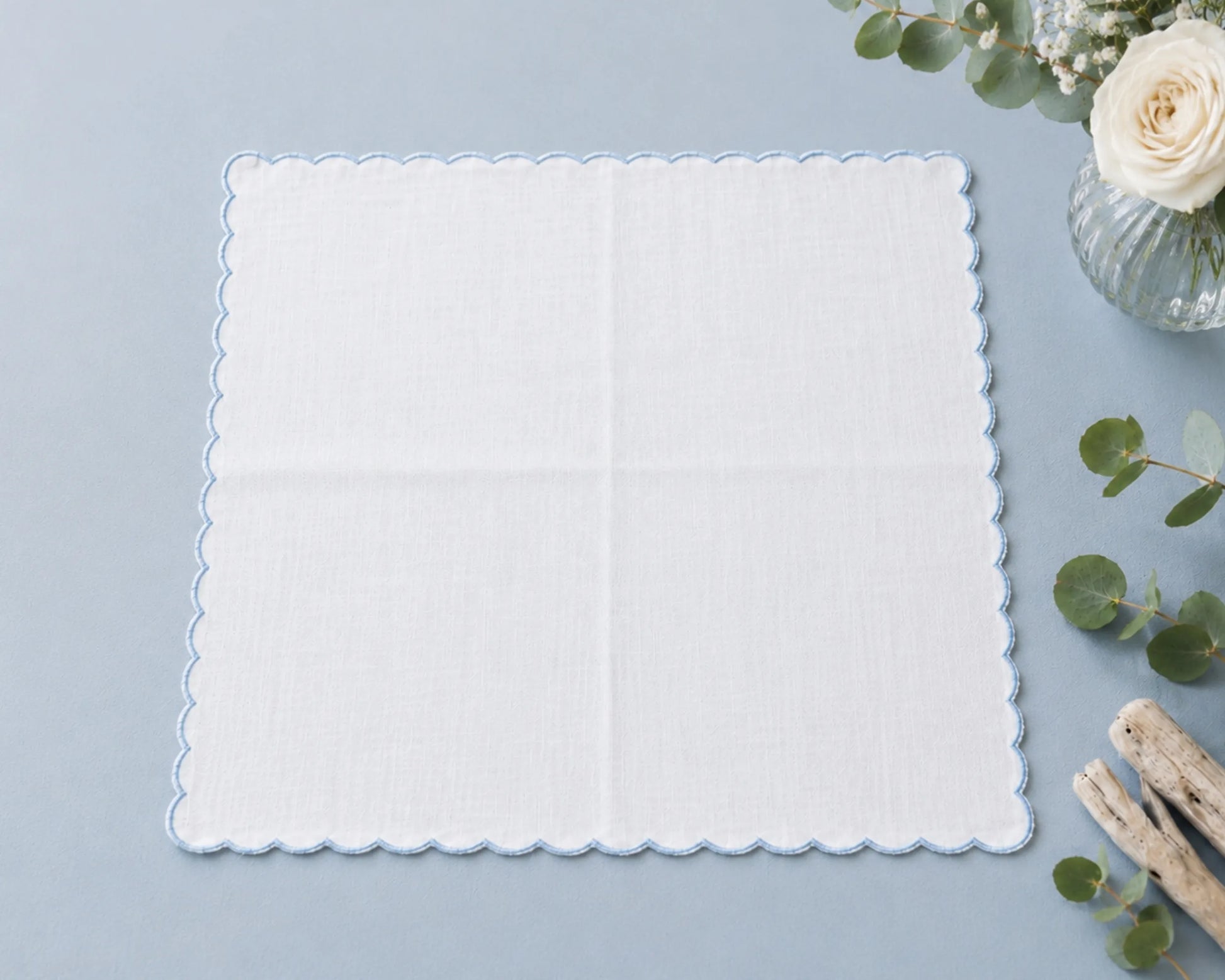 White scalloped-edge hanky on a light blue background with decorative elements.