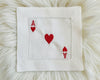 A single white cotton hemstitch napkin featuring a large center heart and "A" symbols for the Ace of Hearts in vibrant red machine embroidery.