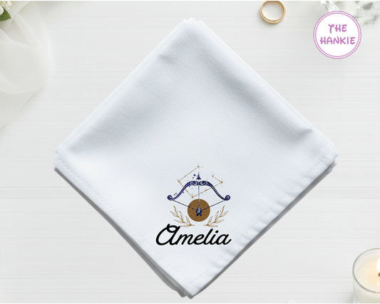 A crisp white cotton handkerchief personalized with "Amelia" below an indigo and gold Sagittarius bow and arrow icon.