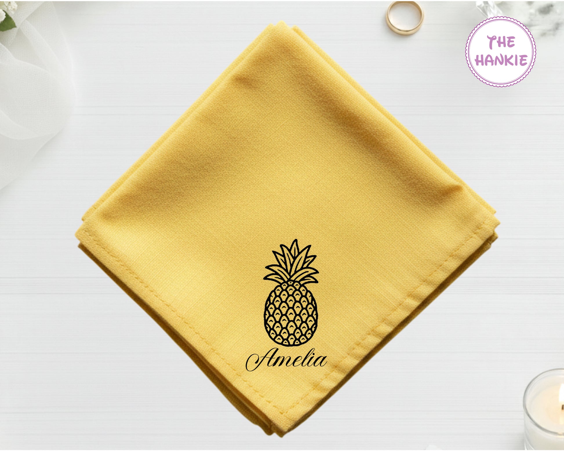 A golden harvest yellow cotton handkerchief featuring the name "Amelia" below a detailed black-threaded whole pineapple illustration.