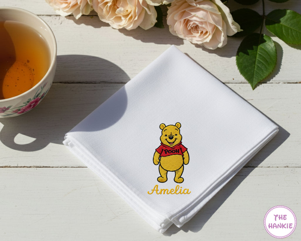 A crisp white cotton handkerchief customized with the name "Amelia" and a detailed embroidery of the classic Winnie the Pooh character.