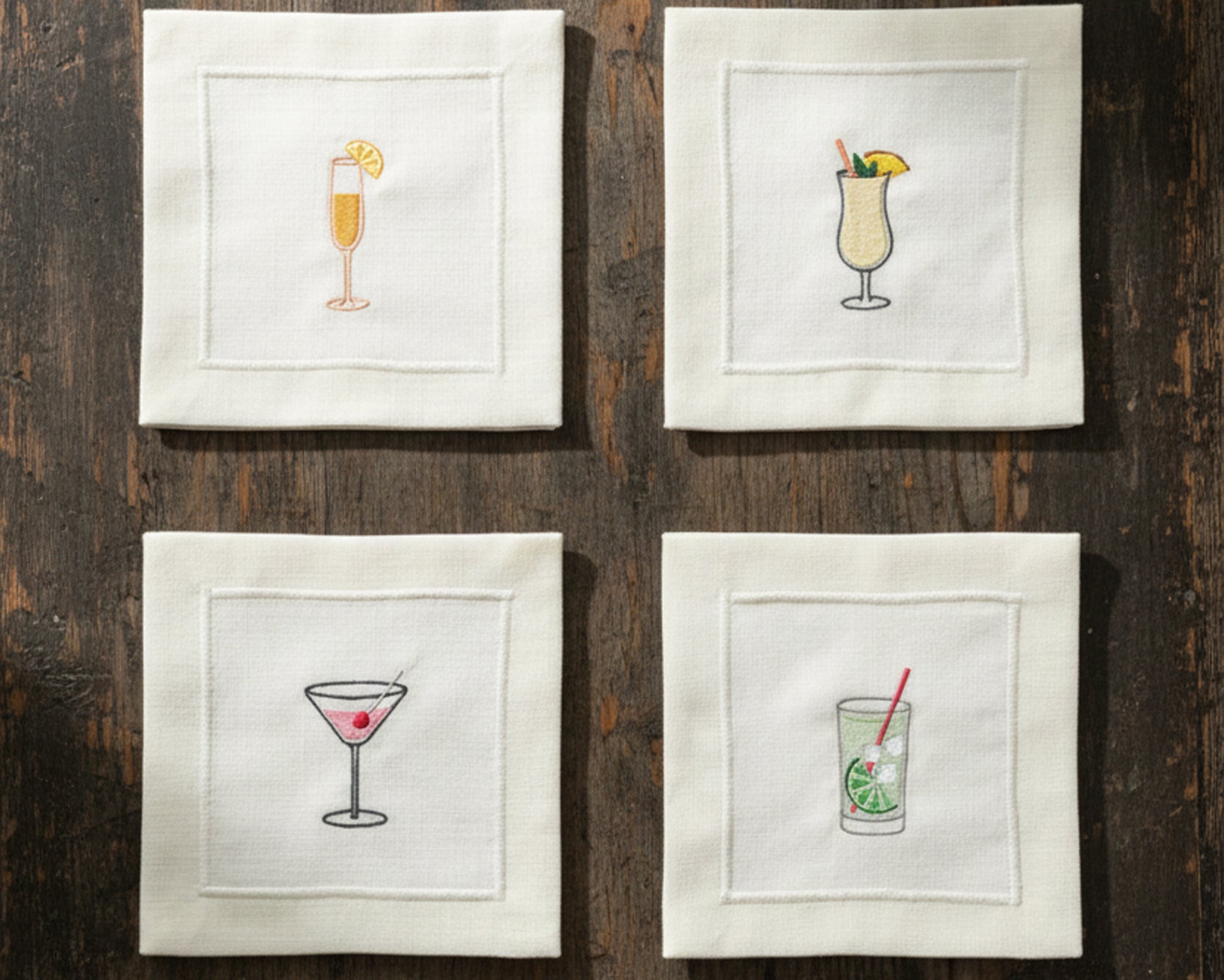 A variety of cream cotton napkins featuring embroidered icons of a Pina Colada, Gin & Tonic, and Espresso Martini.
