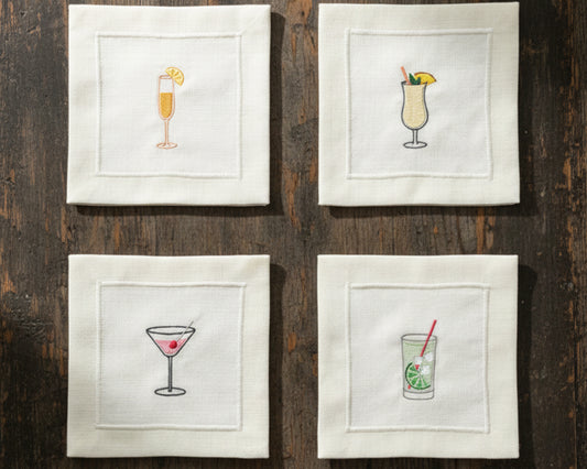 A variety of cream cotton napkins featuring embroidered icons of a Pina Colada, Gin & Tonic, and Espresso Martini.