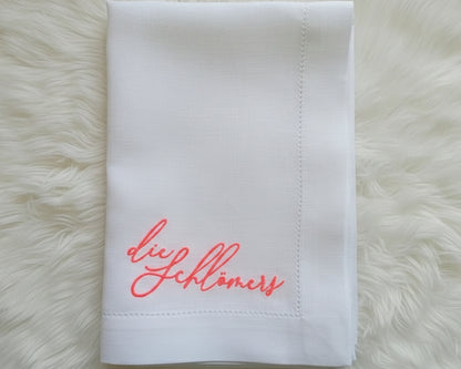 Overhead view of a custom hemstitch linen napkin on a white dinner plate, styled for a modern formal event or wedding