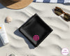 A black luxury satin handkerchief featuring a personalized pink vinyl circular monogram "AA" displayed on a white sand beach.