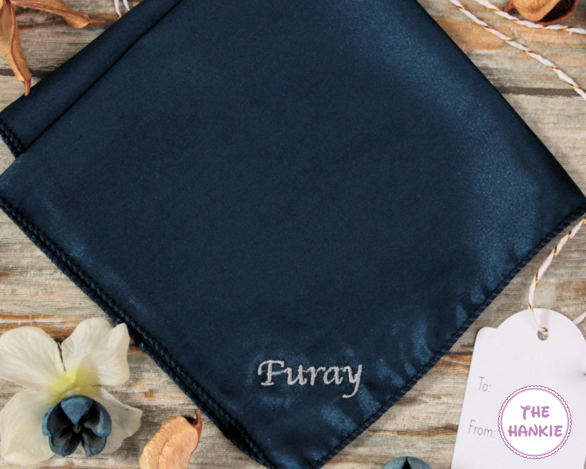 Navy satin hankie with 'Furay' branding on a wooden surface with flowers and a tag.