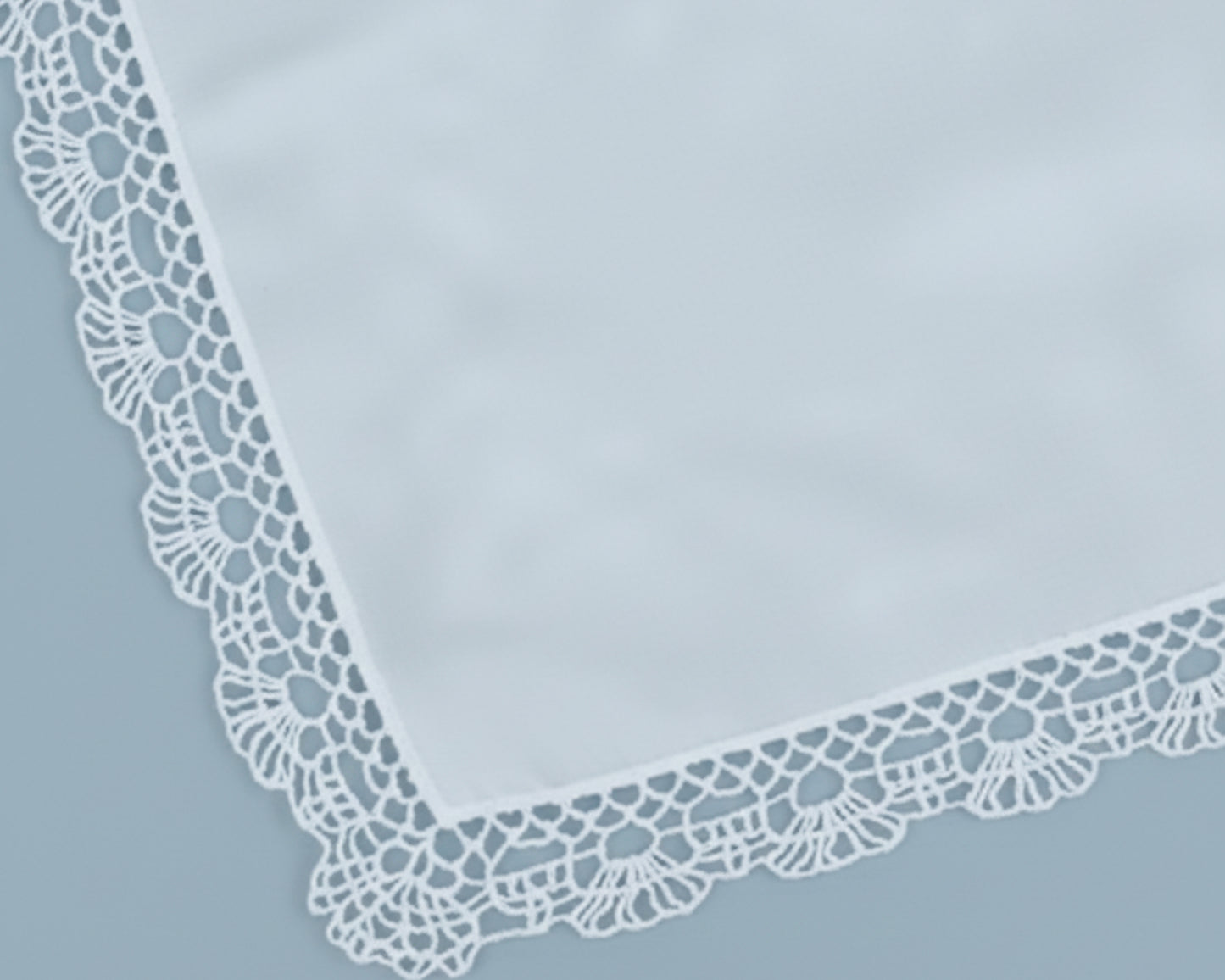 Close up corner view of a soft sky blue cotton handkerchief with a scalloped lace border.