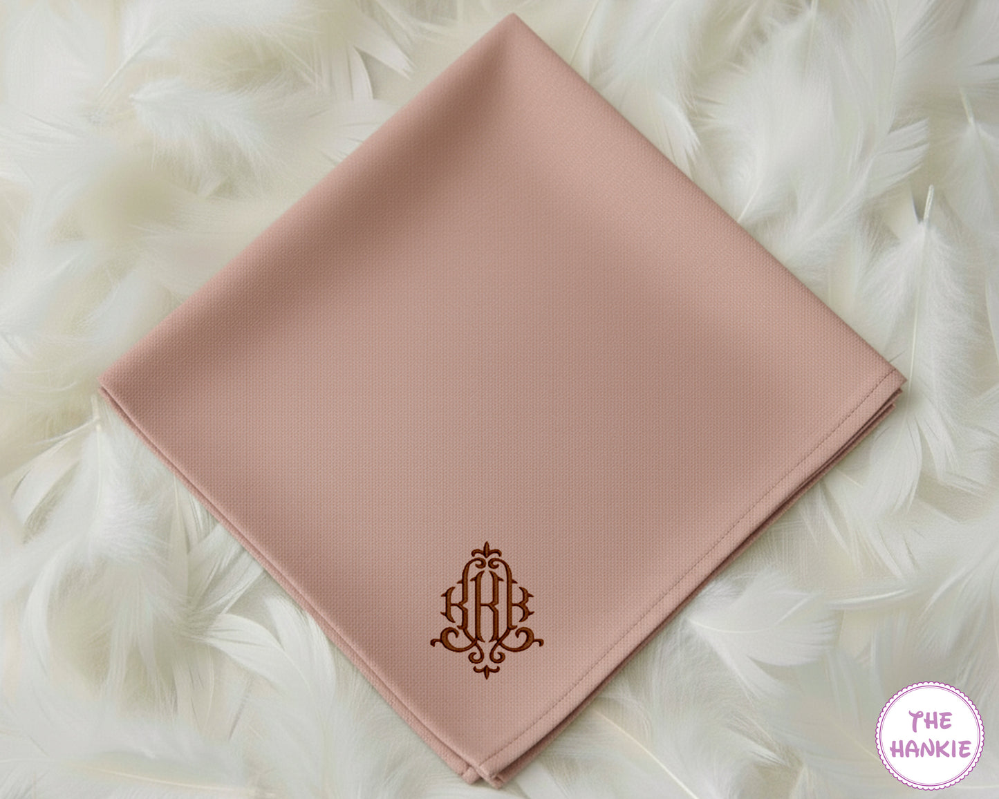 A dusty blush pink premium cotton handkerchief featuring an ornate, classically styled three-initial monogram in a contrasting espresso brown thread.