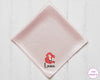 Pink satin square with a character design and text on a white wooden surface, branded 'The Hankie'.