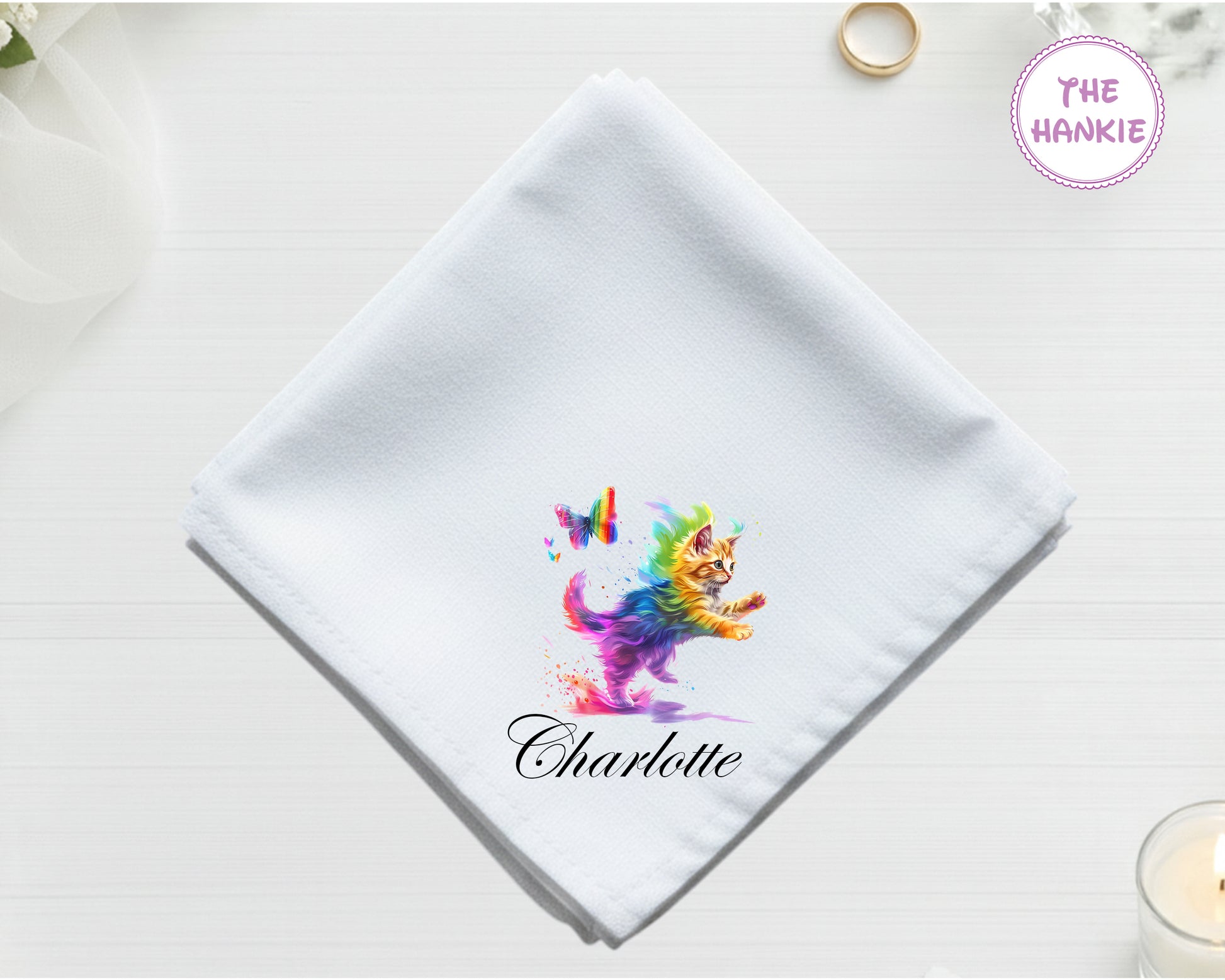 A crisp white cotton handkerchief featuring the name "Charlotte" and a whimsical multi-colored kitten leaping toward a rainbow butterfly.