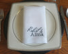 Place setting with a napkin featuring 'Robert & Alma' on a wooden table.