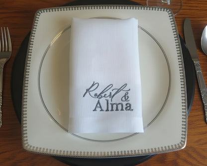 Place setting with a napkin featuring 'Robert & Alma' on a wooden table.
