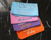 Four personalized bachelorette bandanas with script embroidery displayed on a soft white feather background.