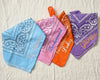 Four personalized bandanas in blue, pink, orange, and purple showing "Mrs. Williams" and "Bridesmaid" embroidery