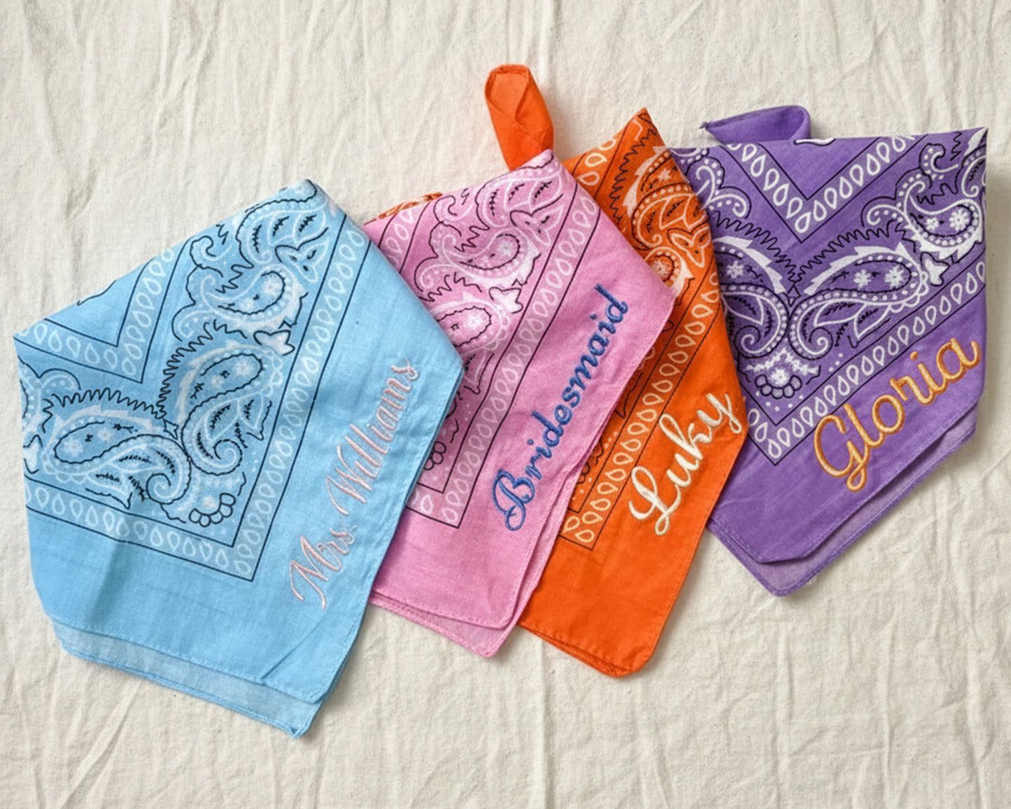 Four personalized bandanas in blue, pink, orange, and purple showing "Mrs. Williams" and "Bridesmaid" embroidery