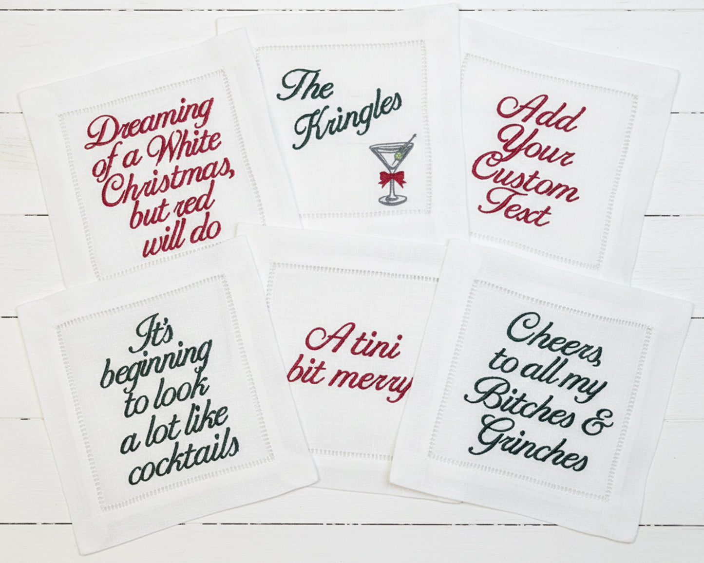 Six white hemstitch napkins featuring festive red and green holiday-themed text and cocktail embroidery.