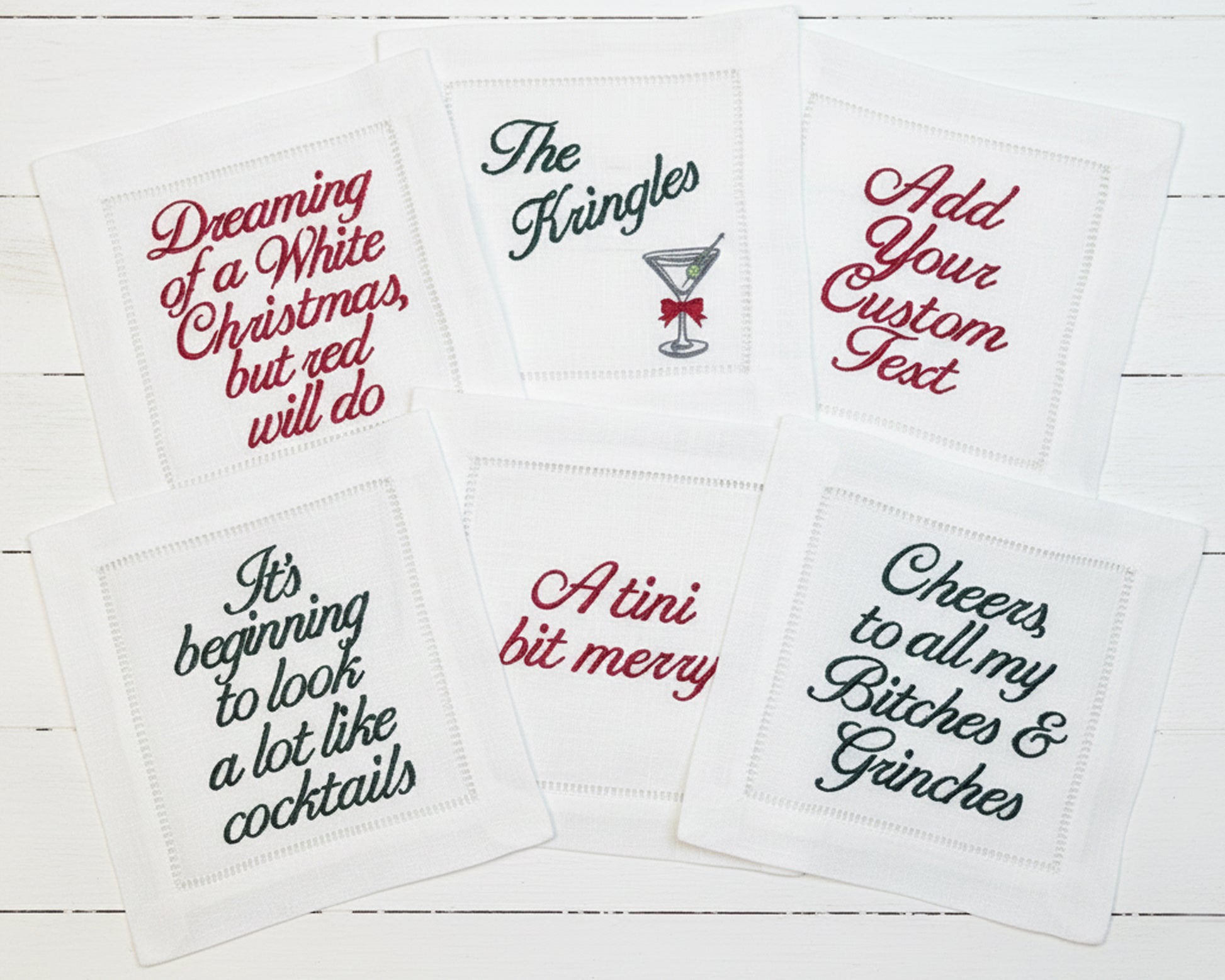 Six white hemstitch napkins featuring festive red and green holiday-themed text and cocktail embroidery.