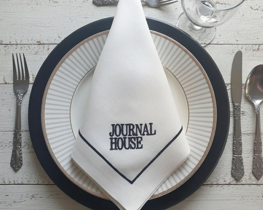 Napkin with 'Journal House' logo on a table setting with plates and cutlery.