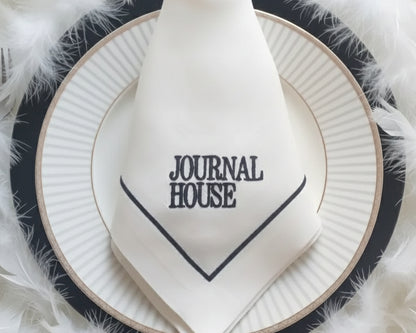 White napkin with 'Journal House' text on a black and white plate with feathered background